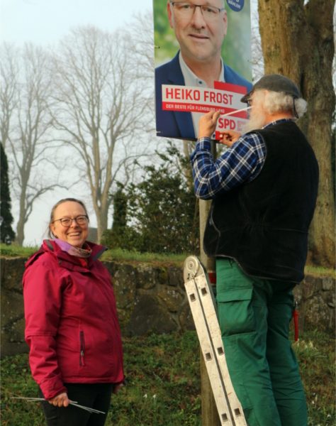 Brigitta & Haiko hängen Wahlkampfplakat von Heiko Frost, Landtagswahl SH 2022, auf