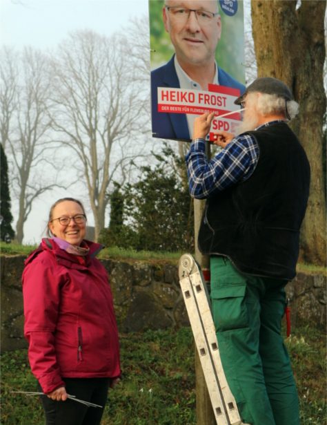 Brigitta & Haiko hängen Wahlkampfplakat von Heiko Frost, Landtagswahl SH 2022, auf